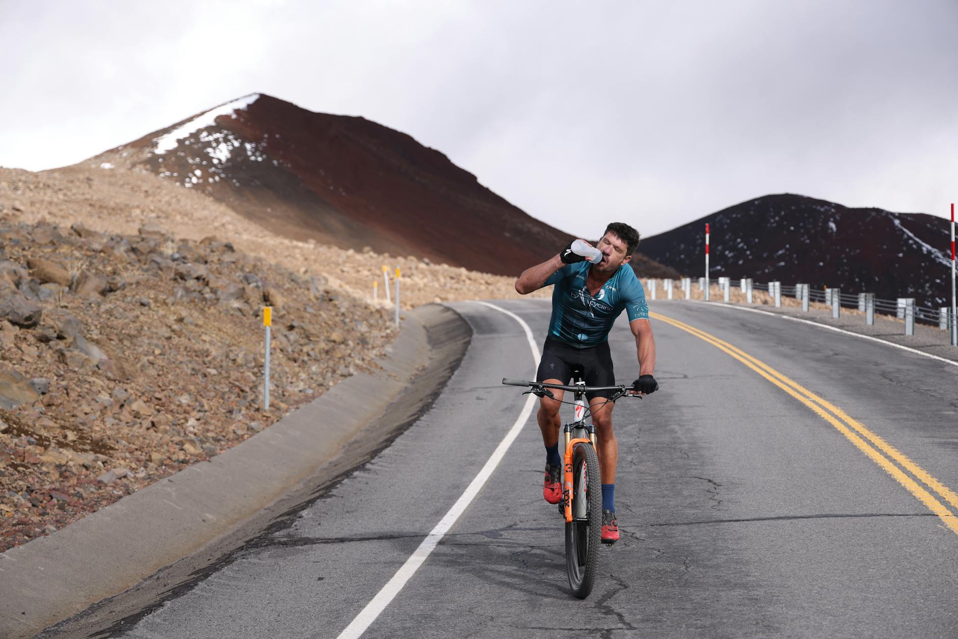 Kolarz na szosie w górach pije wodę podczas podjazdu