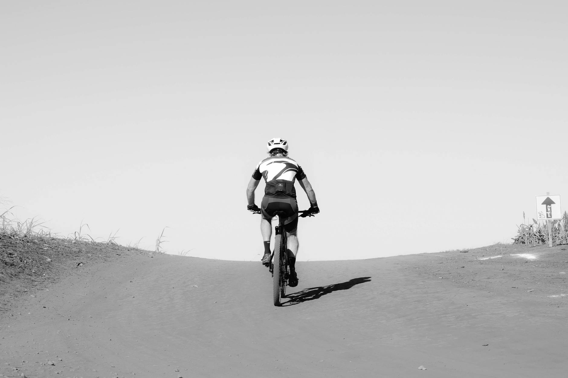 Kolarz podjeżdżający rowerem szosowym pod górę po szutrowej ścieżce