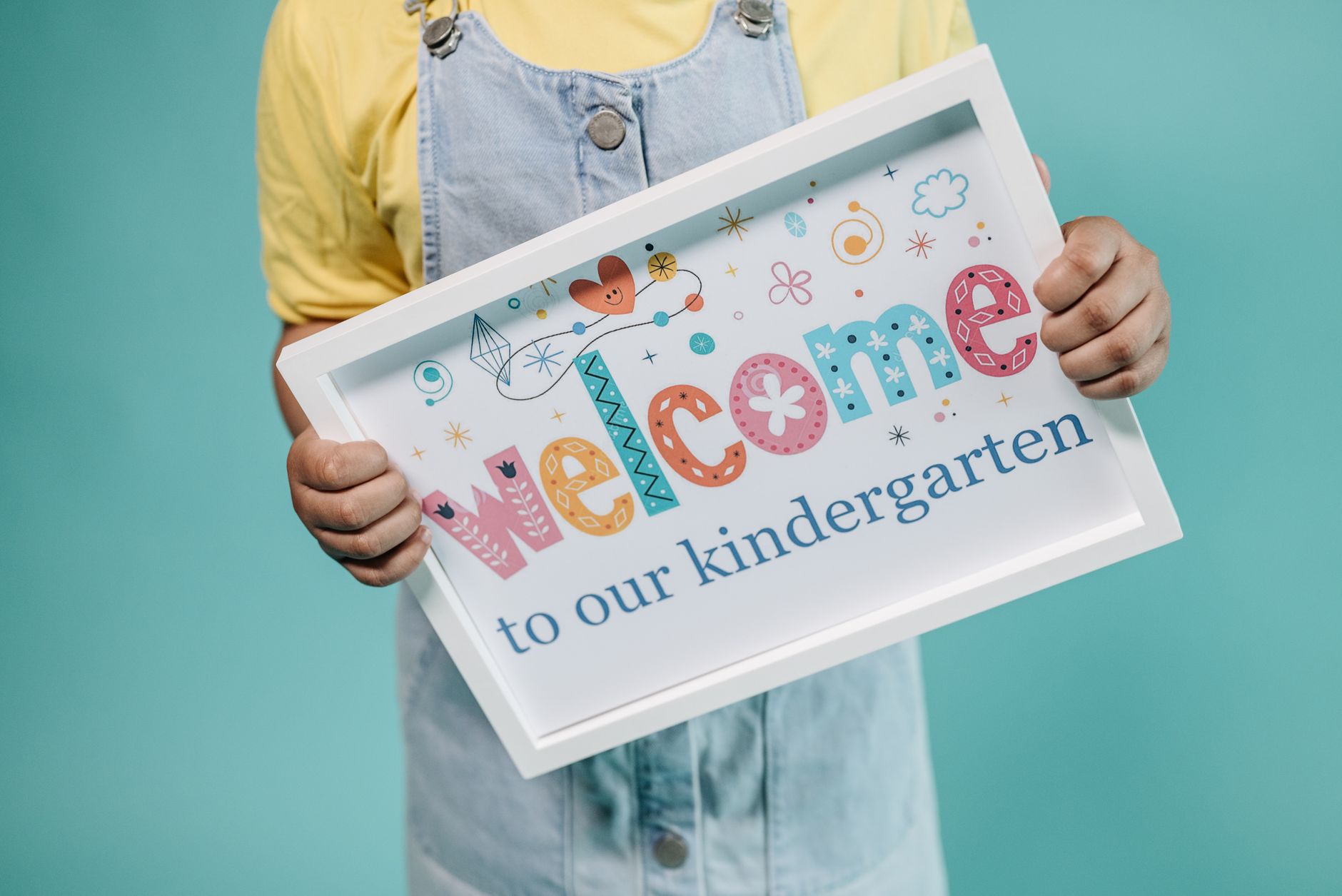 Dziecko trzyma kolorowy plakat welcome to kindergarten na turkusowym tle